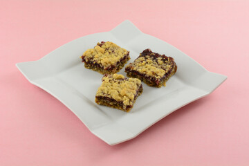 Three baked raspberry oat crumble squares on white dessert plate on pink background