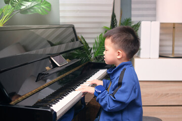 Asian kindergarten school boy child learning to play piano using smartphone with an online lesson and course in living room at home, Children and Music, Benefits of Music in Child Development concept