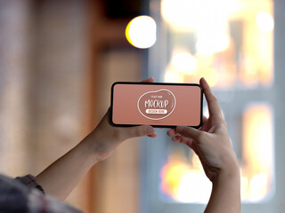 Female hands holding mock up horizontal smartphone screen in  blurred background