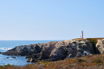 Fototapeta na wymiar Lighthouse over the cliff near a beach
