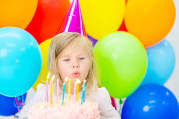 Obraz premium Little girl wearing party's cap blowing candles on birthday cake