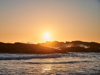 sun setting behind the rock on the sea, with waves splashing