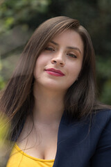 Fototapeta premium face of young white-skinned Latin woman with long, straight hair, light eyes and makeup, smiling, looking straight ahead, wearing a yellow blouse and blue jacket, photo in natural daylight