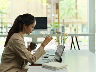 Side view of female working with digital tablet and drinking coffee in office room
