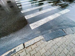 white zebra pedestrian crossing after heavy rain. rainy background with water flows and sky reflections