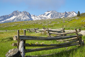Fototapeta na wymiar Mountain peaks rising out of green pastures with a rustic wood fence on a beautiful summer day