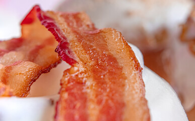 Delicious cinnamon roll with piece of bacon on top and pink background.