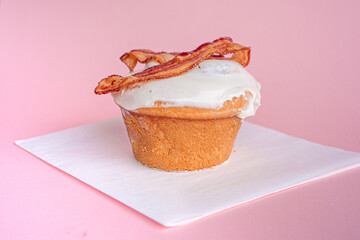 Delicious cinnamon roll with piece of bacon on top and pink background.