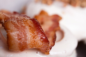 Delicious cinnamon roll with piece of bacon on top and pink background.