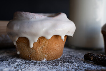 Homemade cinnamon roll with white glaze a bottle with milk and a piece of cinnamon in front of it.
