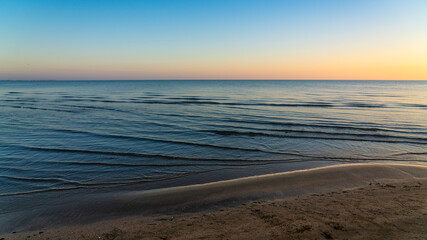 Sandy seashore with small waves before sunrise
