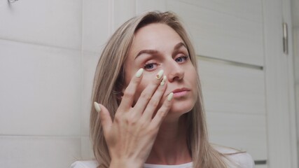 Woman applying cream under the eyes and looking at the camera