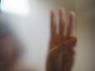 A woman raises three fingers to express peace and freedom, which is displayed behind a tarnished frosted glass. No one saw
