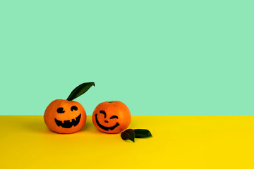 Little mandarines with painted faces for Halloween on yellow and green background