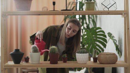 Young woman holding red watering can waters house plants in pots