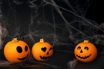 Little orange pumpkins with painted faces for Halloween with spiders on the net on black background