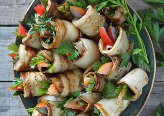 Vegetable rolls with spicy grass on a wooden background.A dish of tomatoes wrapped in fried eggplant wedges.