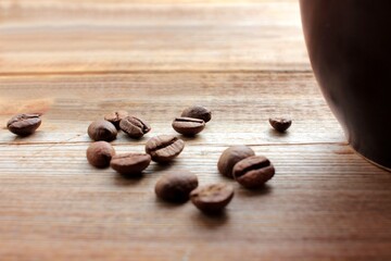 Roasted coffee beans near the cup on wooden table background with copy space. Rustic style
