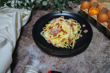 Spaghetti Carbonara in black plate on table in restaurant.