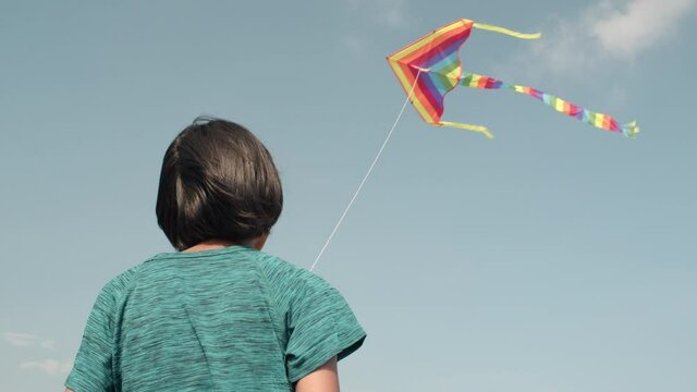 Happy Asian girl is playing rainbow kite flying on blue sky joyful 