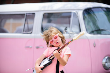 Portrait of a funny child with pink glasses practicing a song during a guitar lesson on street. Music concept, kids music school. Rock concert.