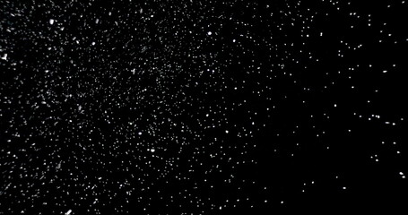 White snowflakes falling in slow motion against an isolated black background.