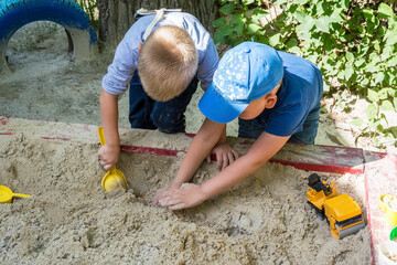 Little boys play in the sandbox. Building a garage for a toy car.