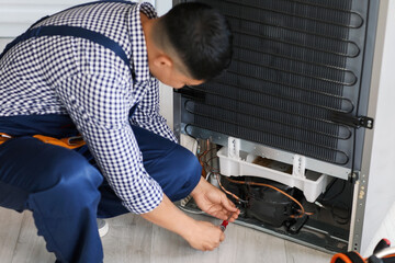 Worker repairing fridge in kitchen