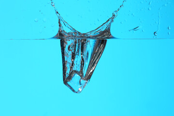 Falling of ice cube into water on color background