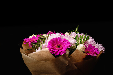 Large beautiful bouquet of chrysanthemums, gerberas, roses and ferns in pink and purple colors, packed in brown craft paper and isolated on a black background. Postcard for the holiday.