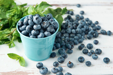 Blue bucket with blueberry and mint leaves on white Provence style wooden table.