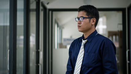 A young Asian businessman wearing glasses and standing by the mirror