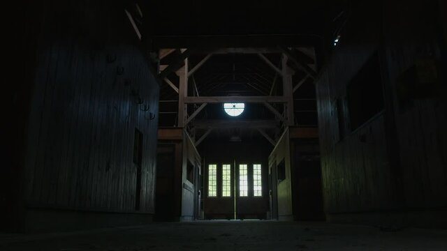 Daylight pours through doors into dim and unused horse stable or equestrian barn