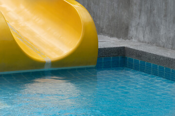 yellow slider with blue swimming pool in summer time recreation background