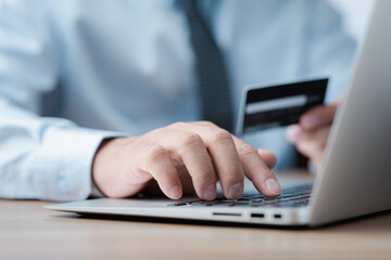 Close up of businessman hands holding a credit card and making a purchase using a laptop.