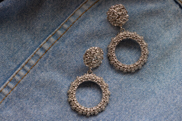 silver large earrings on the background of light blue jeans
