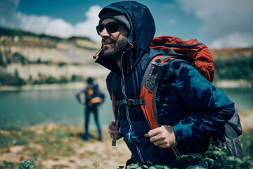 Attractive bearded man holding his backpack and exploring nature on a camping trip.