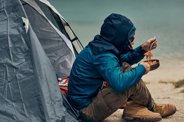 Man sitting next to tent and eating his lunch on a camping trip.