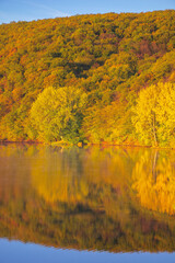 mountain lake among the forest. trees in colorful foliage. beautiful landscape on a sunny autumn morning. blue sky reflecting in the water