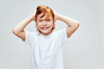 An energetic child with red hair touches the hair on his head with his hands happy childhood