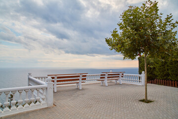 Summer vacation. Ocean panoramic view. Relax vibe. Empty promenade with bench. Stormy sky. Calming sea. Lonely tree