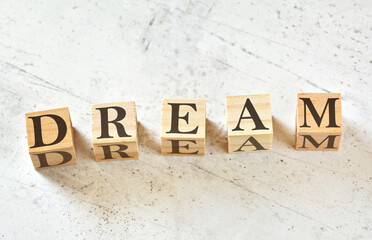 Five wooden cubes with letter DREAM (acronym for Dedication Responsibility Education Attitude Motivation) on white stone like board, view from above