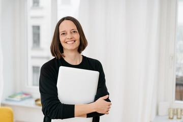 Smiling friendly businesswoman clutching a laptop