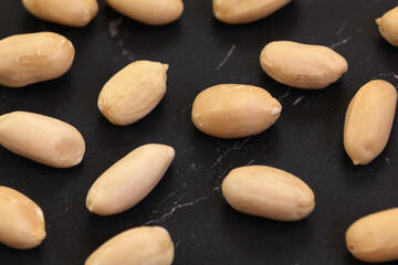 Fototapeta na wymiar Group of peeled peanuts on black marble like board, closeup detail from above