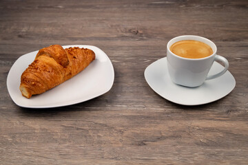 A breakfast with a delicious croissant on a plate and a coffee