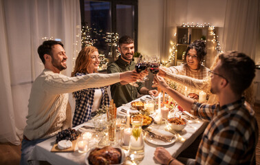 holidays, celebration and people concept - happy friends having christmas dinner at home drinking non-alcoholic red wine