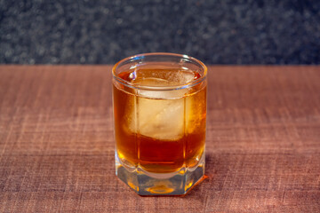 Glass with whiskey or cognac with ice on a wooden surface close up