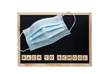 Back to school words lettering on the school black chalkboard. Medical mask on the background of the chalkboard.