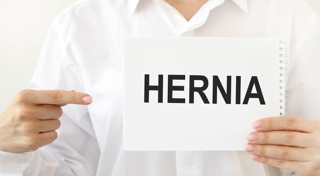 The girl points her index finger on a notebook that says HERNIA.