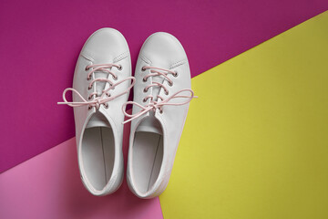 Pair of white gumshoes on pink-yellowl background.